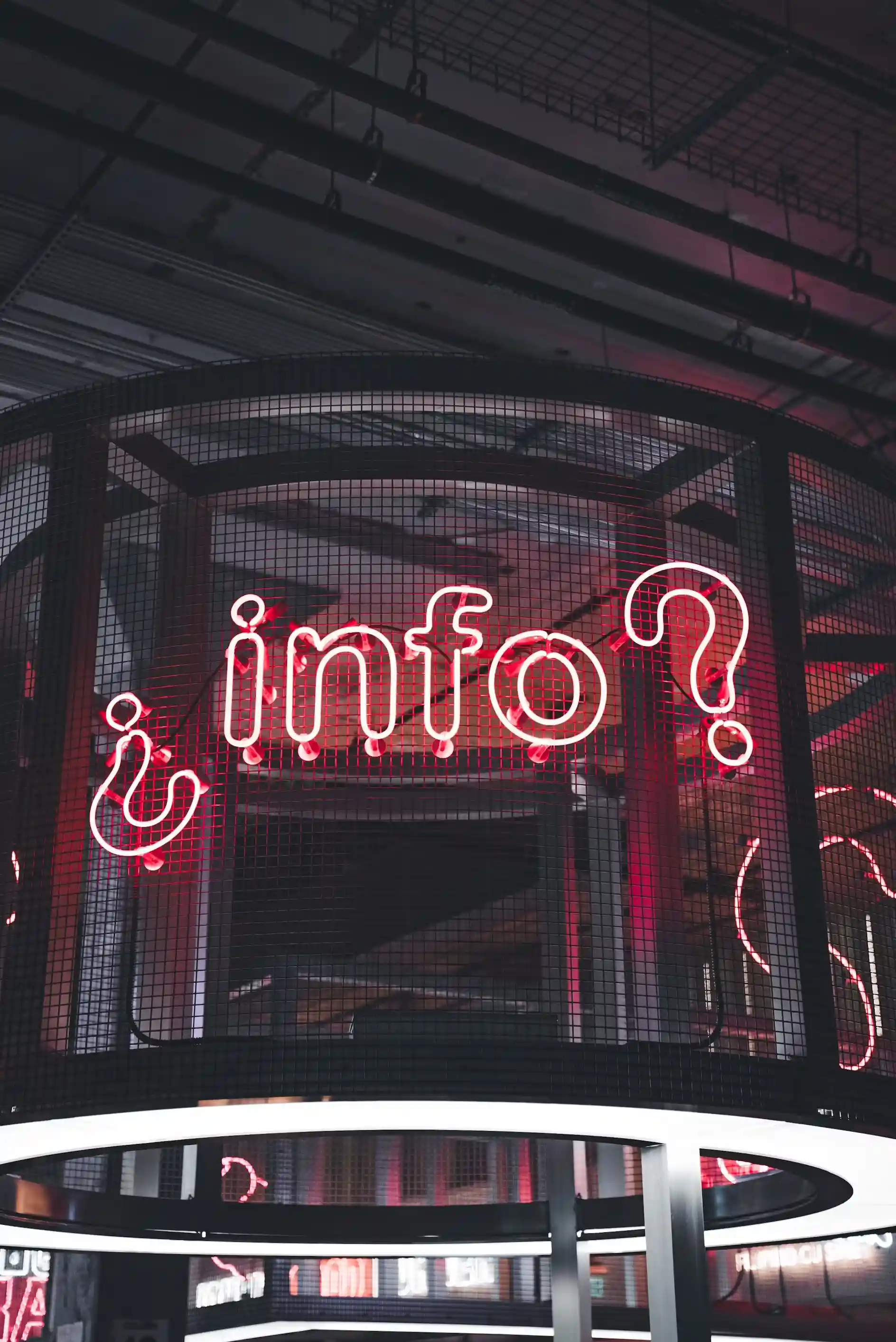 Red neon sign displaying 'info?' with question marks inside a black wire mesh cage.