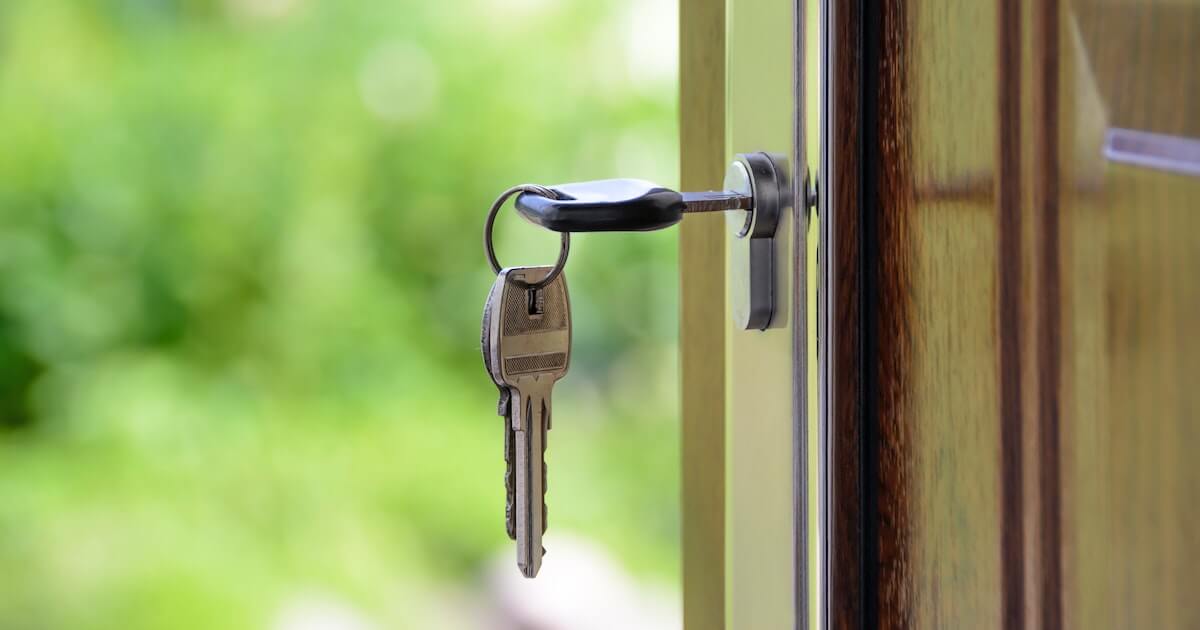 Close-up of a set of keys hanging from a lock in a partially open door, with a blurred green background.