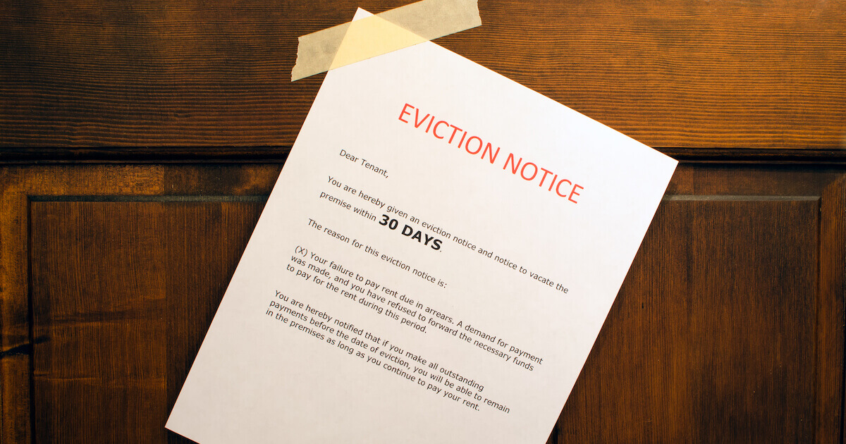 A printed 'Eviction Notice' letter taped to a wooden door, stating a 30-day notice to vacate for failure to pay rent.