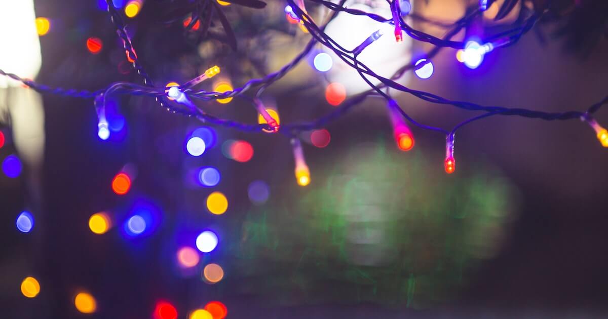 Blurred, colorful string lights in blue, red, yellow, and white against a dark nighttime background.