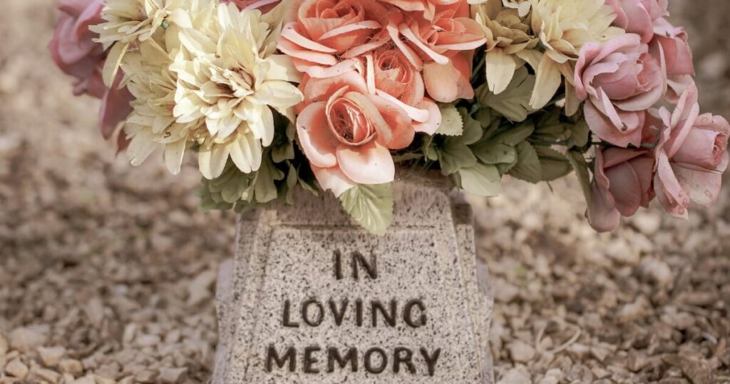 Close-up of a stone memorial marker reading 'In Loving Memory' topped with a bouquet of pink, cream, and peach flowers.