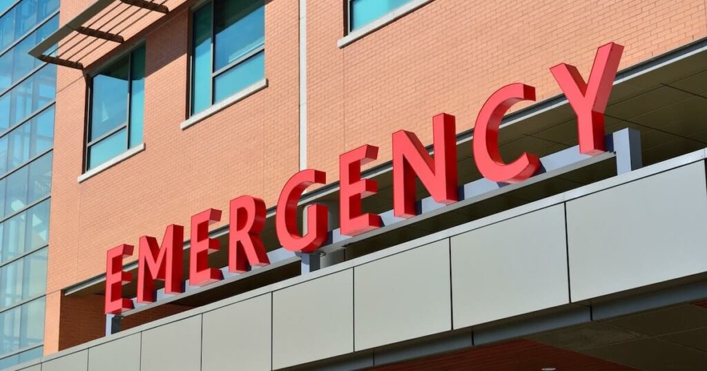 Close-up of a red 'EMERGENCY' sign mounted on a hospital building's exterior.