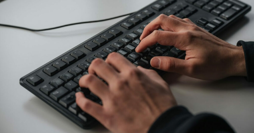 Close-up of hands typing on a black computer keyboard.