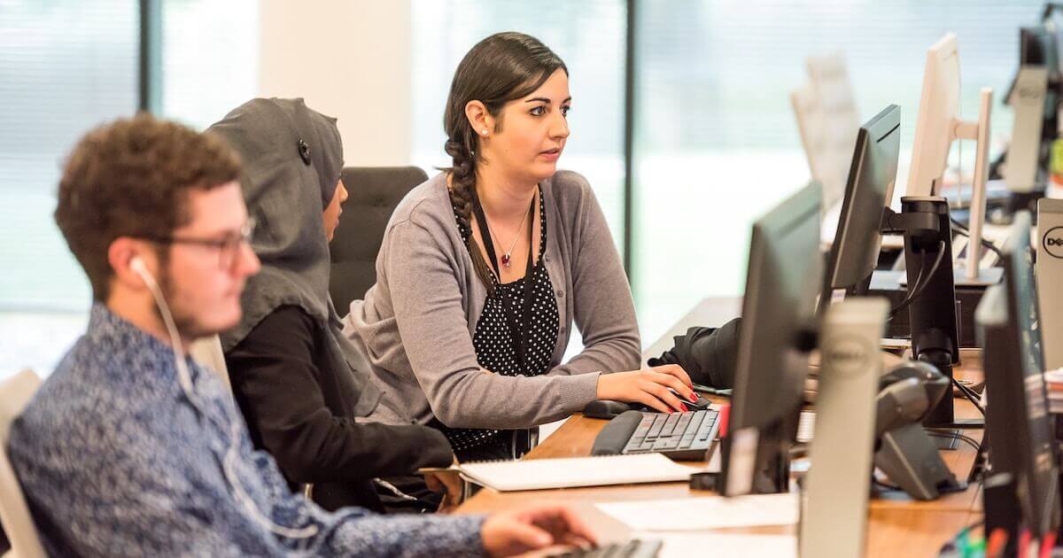 Three colleagues seated next to one another at a long desk, each working on their own computers