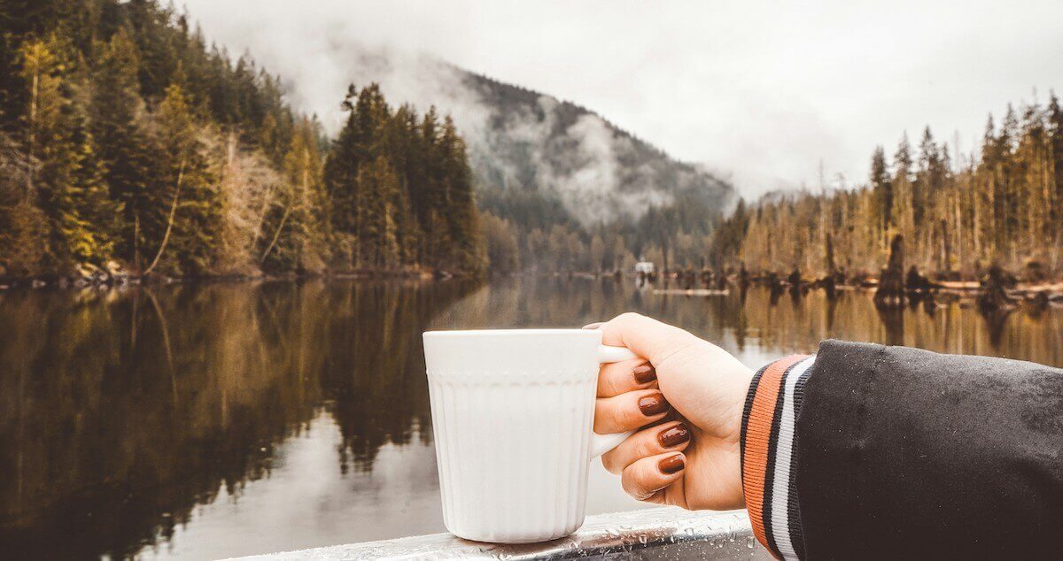A woman's hand holds a white coffee mug while overlooking a serene coastline in Coquitlam, British Columbia
