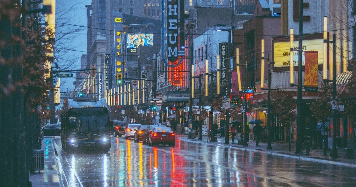 A public transit bus and cars drive down a rainy street in downtown Vancouver at dusk