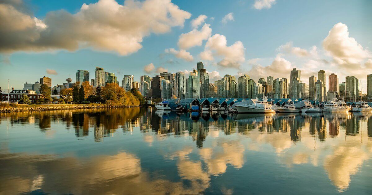 A city skyline and marina reflected in calm harbour water at sunset