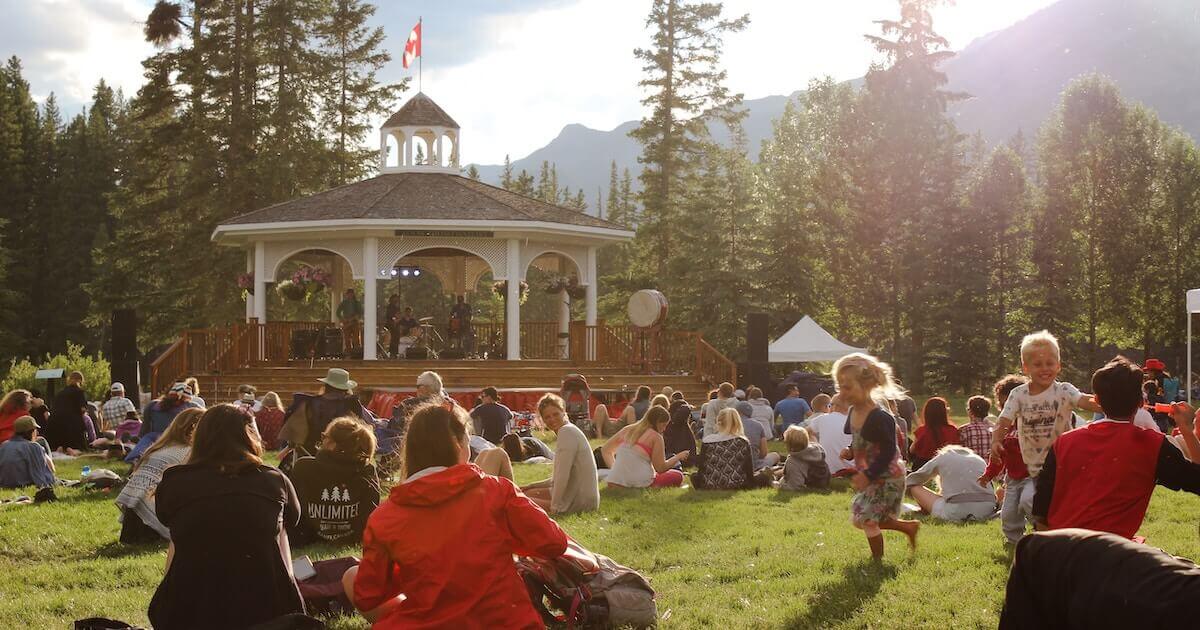 Families gathered, sitting on the grass in a park together during Canada Day celebrations