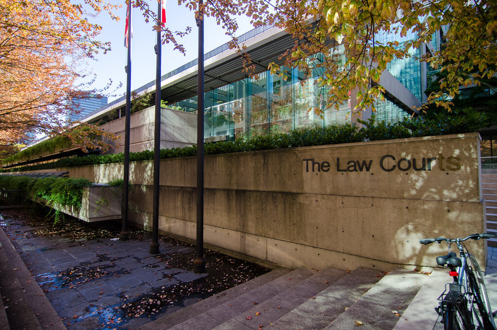 Entrance of the Vancouver Law Courts, framed by autumn trees and flagpoles