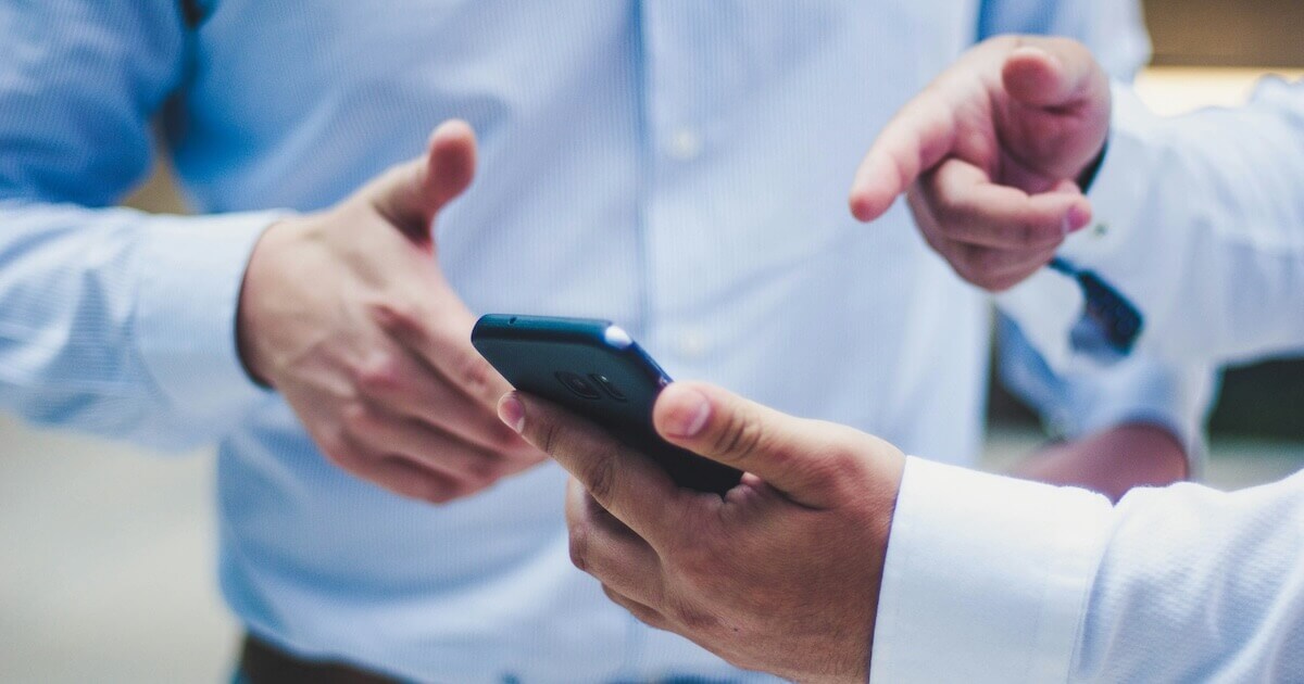 Two male colleagues discuss something one of the men points to on his smartphone