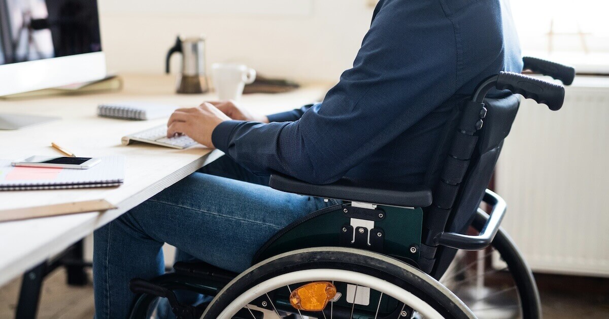 An employee sits in a wheelchair while working on a desktop computer