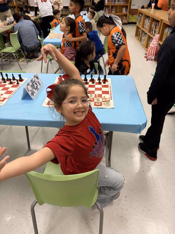 Excited elementary student smiling at a chess board during a scholastic chess event. Shared by RGV Chess and Learning Center.
