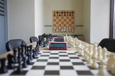 Row of chessboards and digital clocks set up on tables in a classroom.