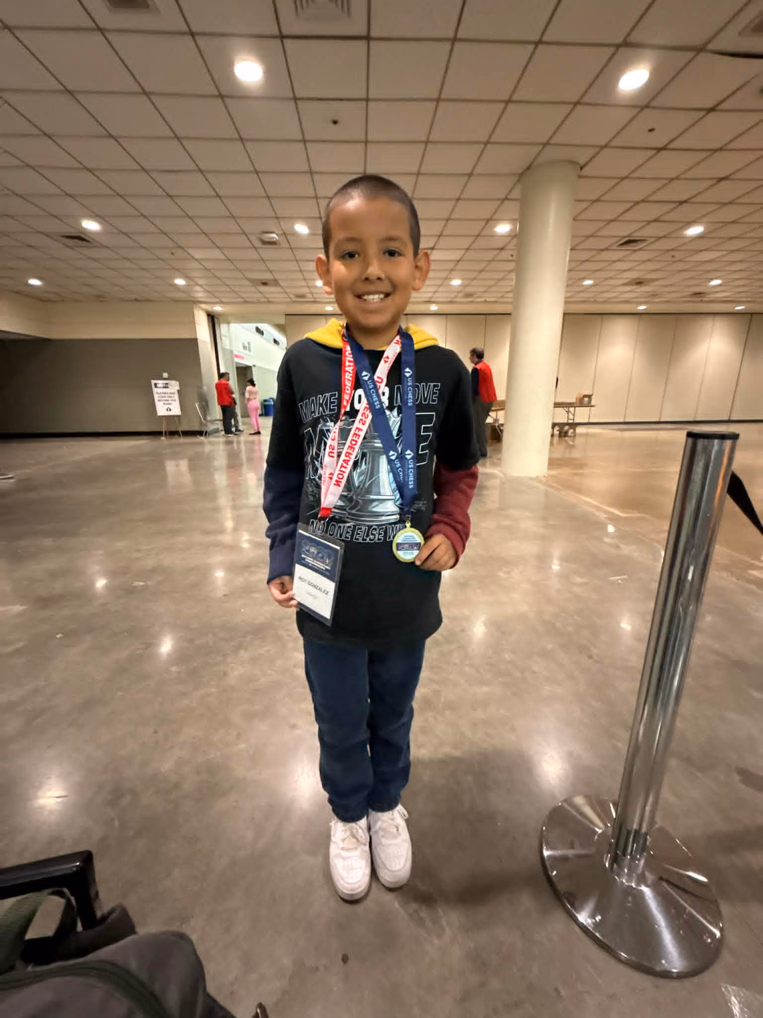 Young chess player proudly wearing his US Chess lanyards and tournament medal at US Chess Nationals with RGV Chess and Learning Center.