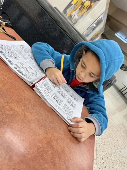 Young student with autism focused on writing and solving chess puzzles in a workbook.  Shared by RGV Chess and Learning Center.