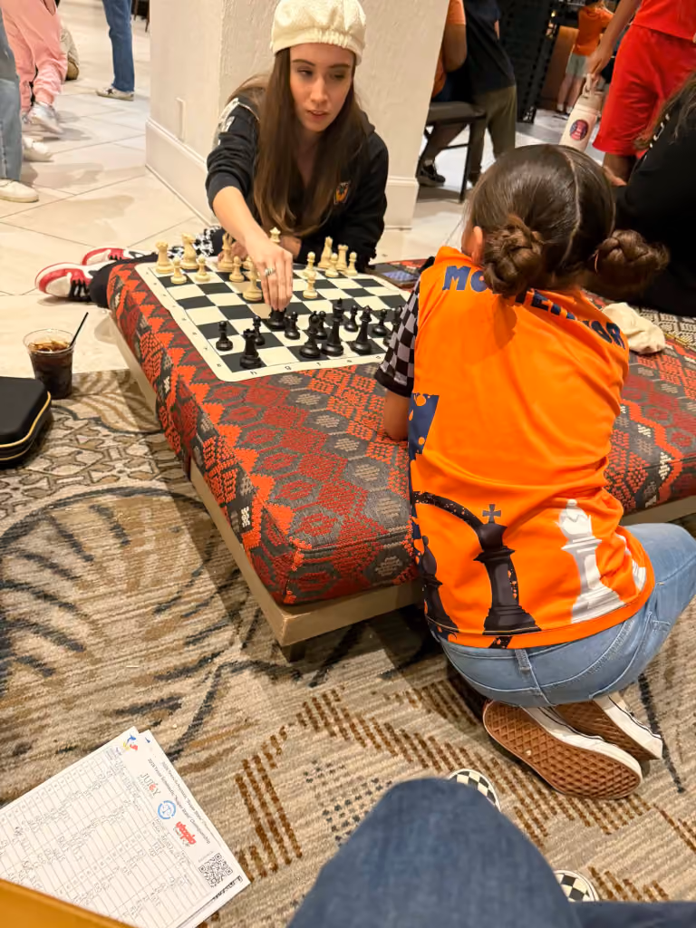 A coach and young student analyzing a chessboard setup together on the floor during a state tournament gathering. Shared by RGV Chess and Learning Center.