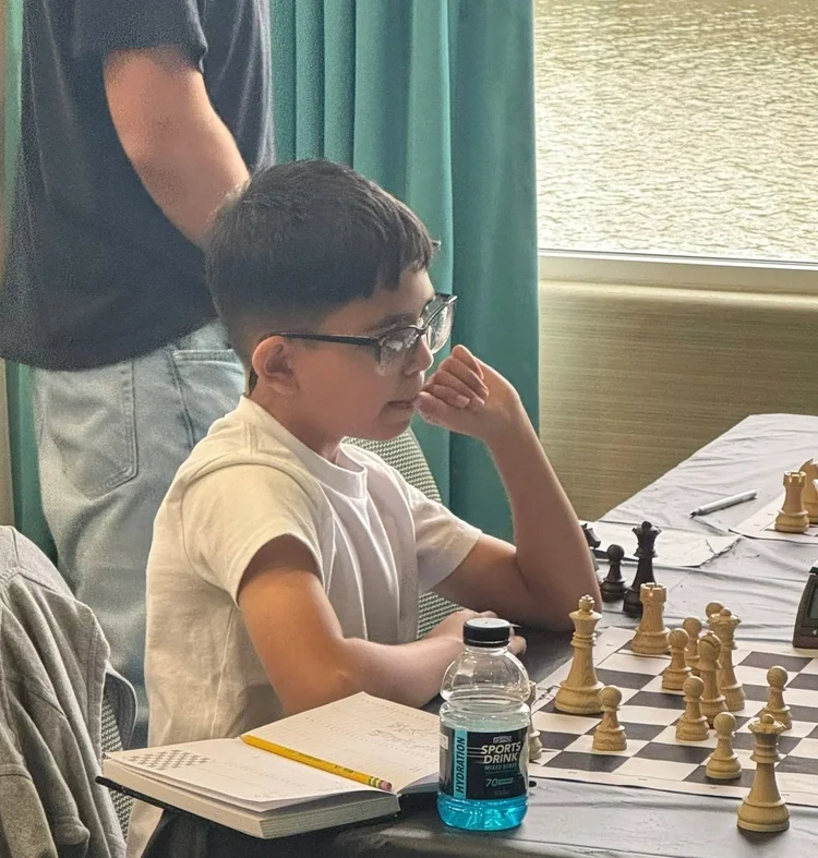 Scholastic chess player concentrating deeply beside his scoresheet notebook during a match. Shared by RGV Chess and Learning Center