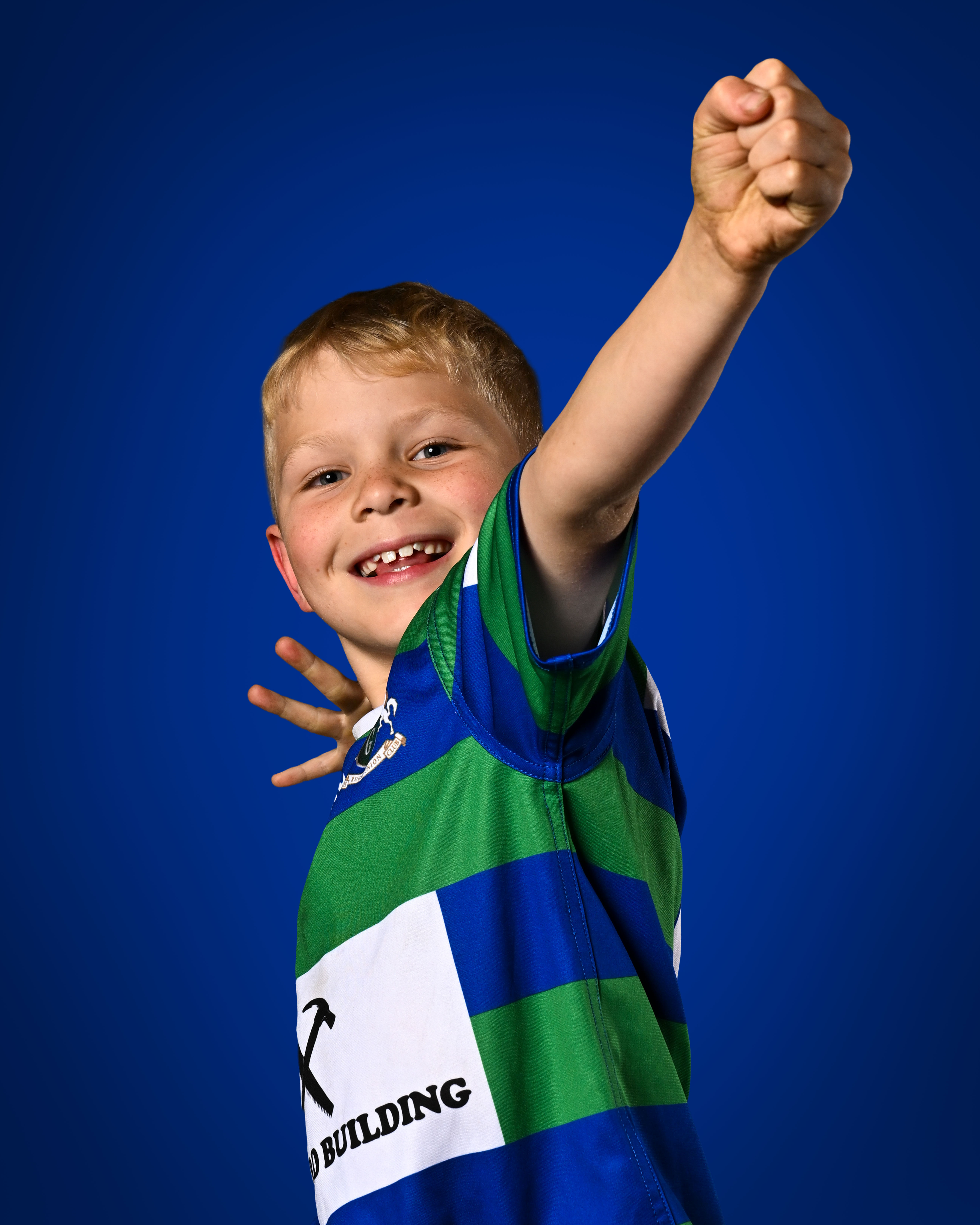 Junior rugby player in a green and blue club jersey with a raised fist against a blue backdrop