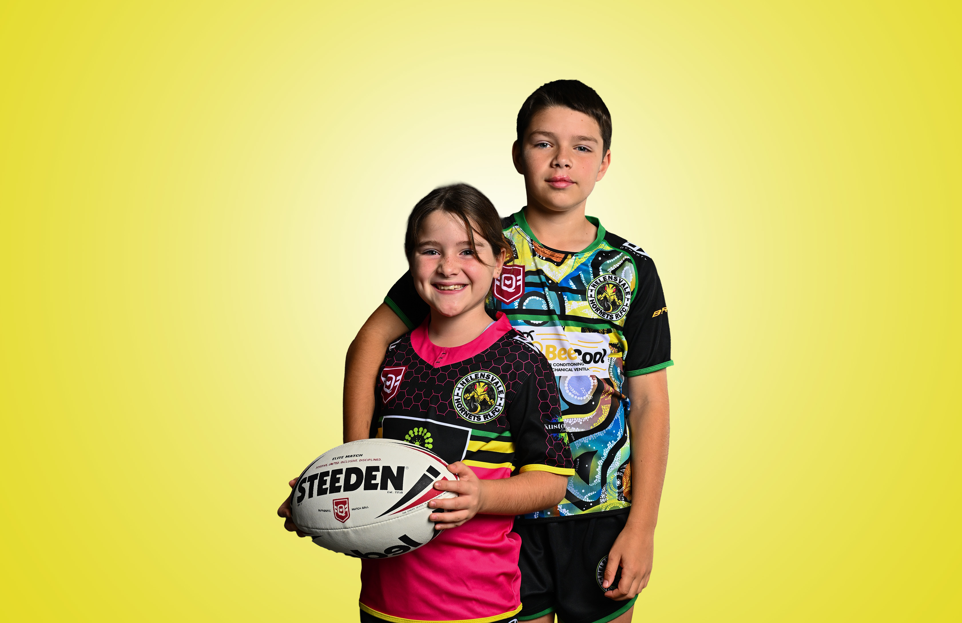 Two junior rugby league players in club uniforms holding a rugby league ball against a yellow backdrop