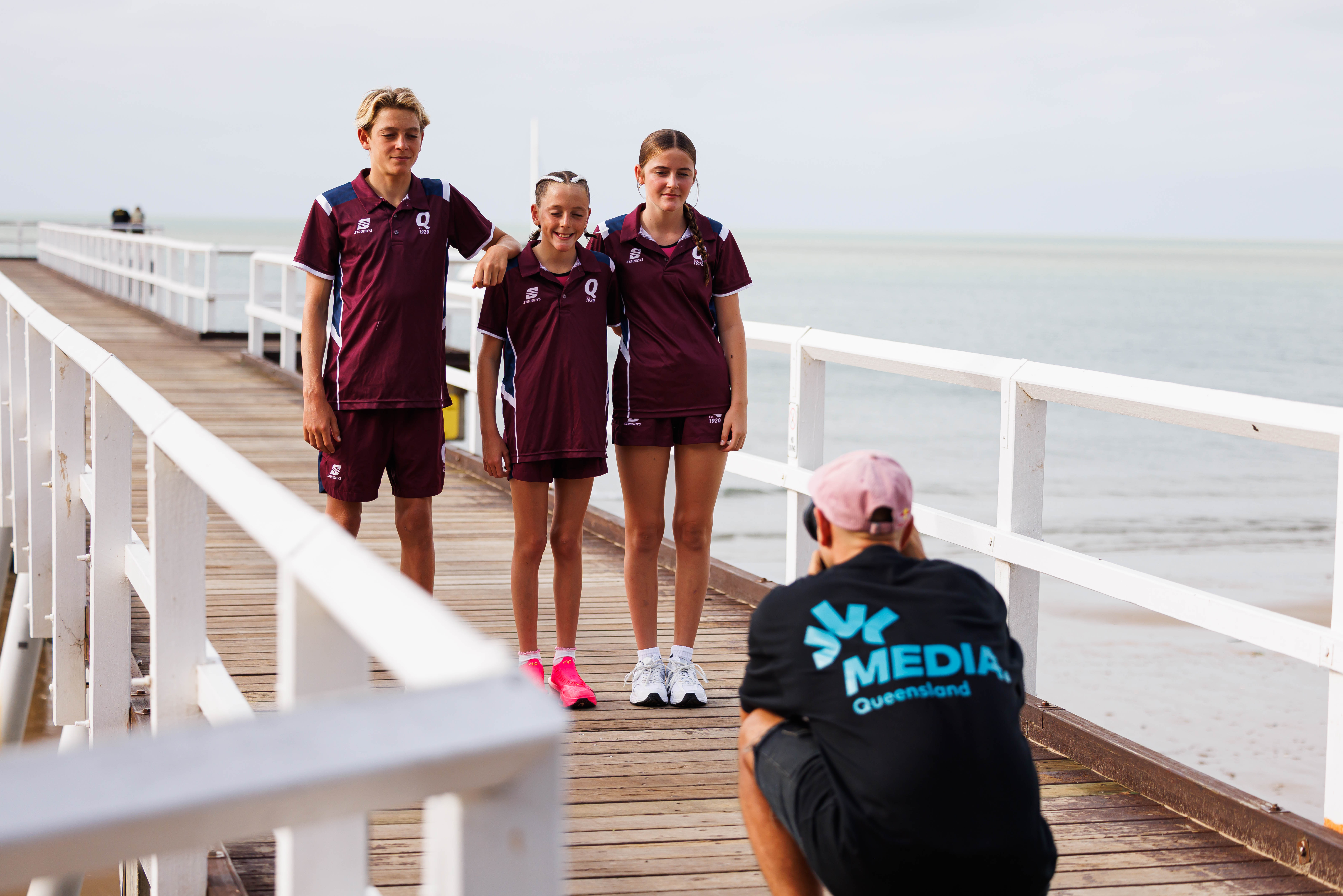 Media Queensland photographer taking a team photo of three junior athletes in club uniforms on a jetty