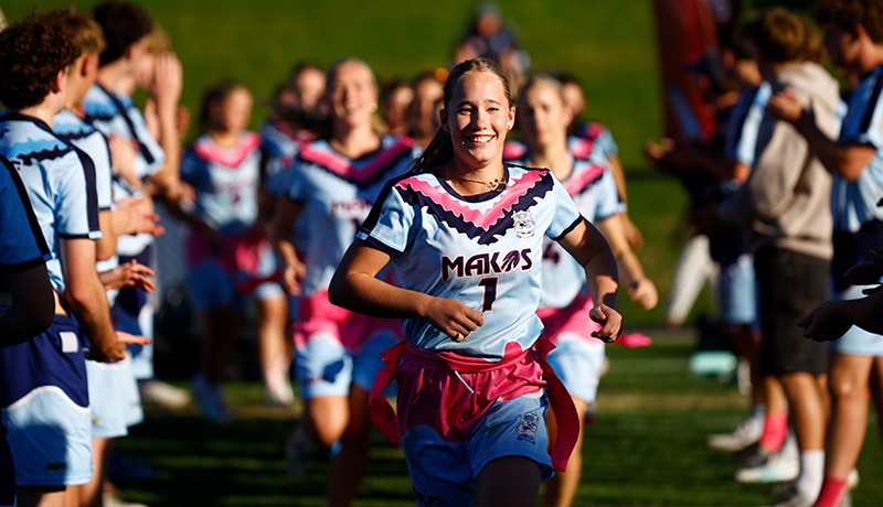 Smiling girl in a pink and blue club uniform jogging onto the field with her teammates behind her