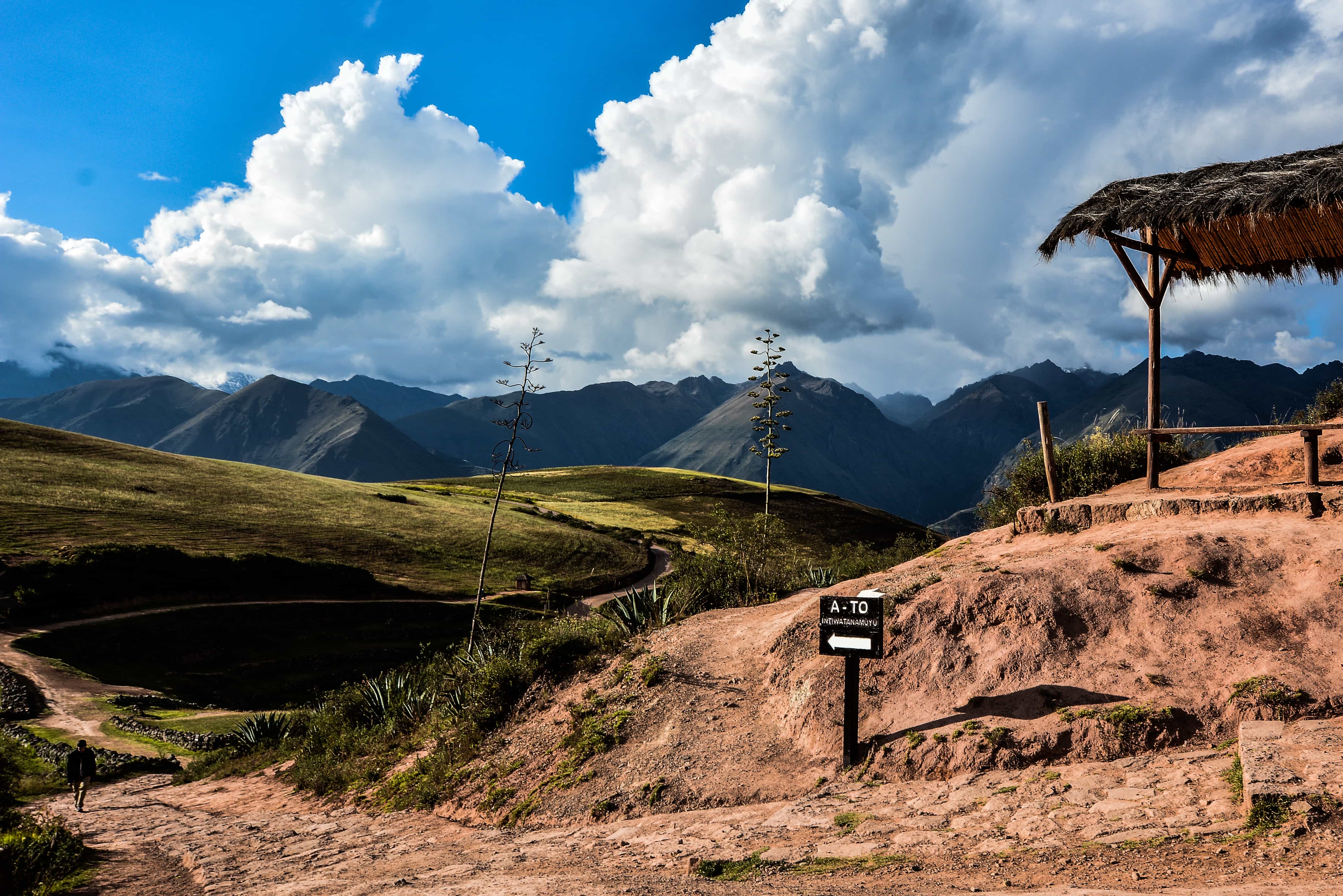 Green mountain valley with a thatched shelter and a trail sign under heavy cloud