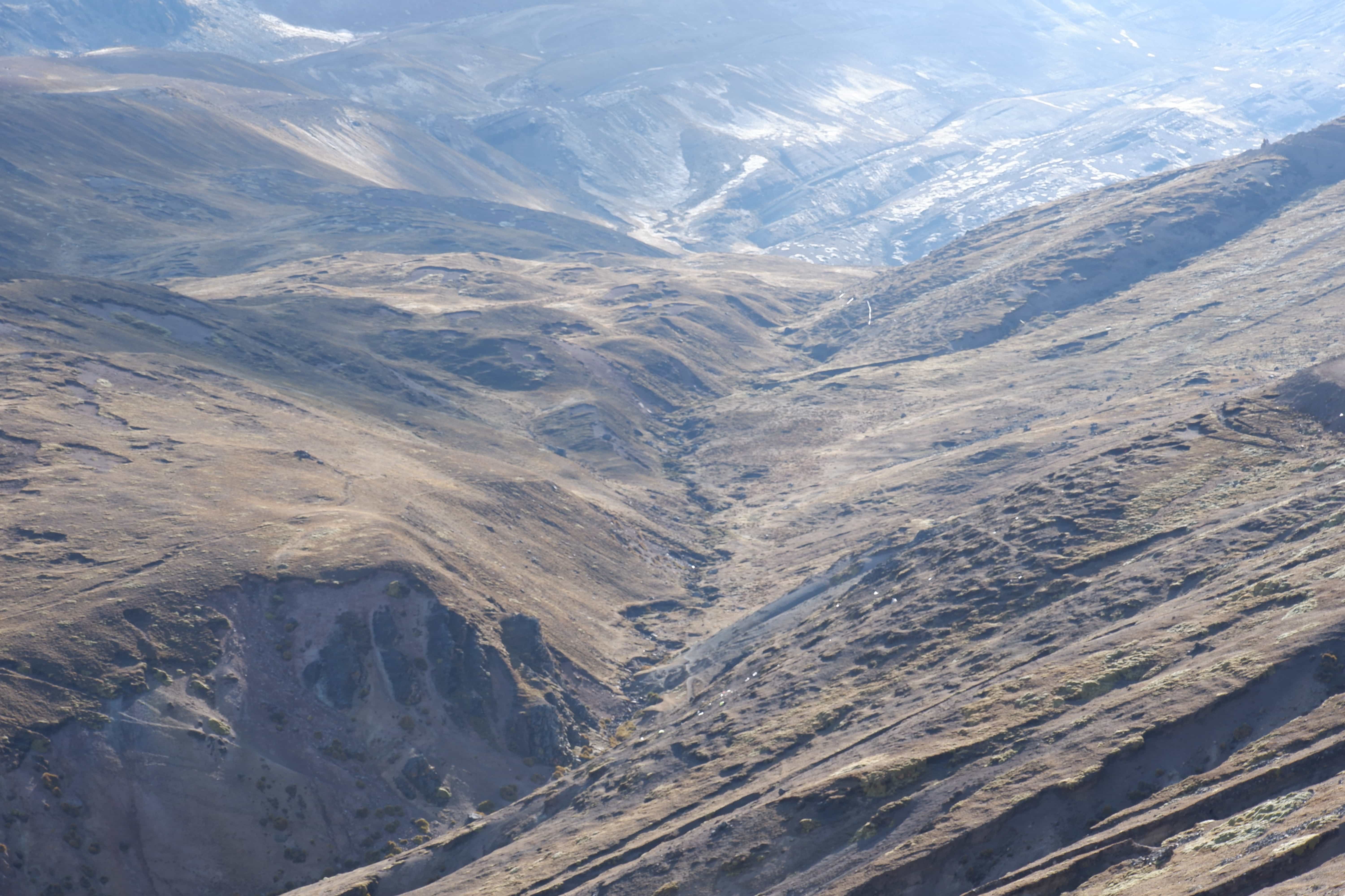 Aerial view of a mountain valley with snow patches and eroded slopes