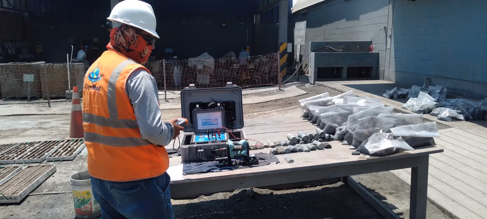 Worker in safety vest and hard hat examining equipment beside rock samples on a table