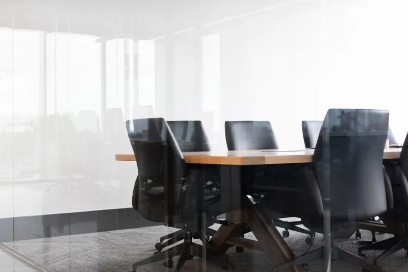 Sala de consejo vacía con una mesa larga y paredes de cristal
