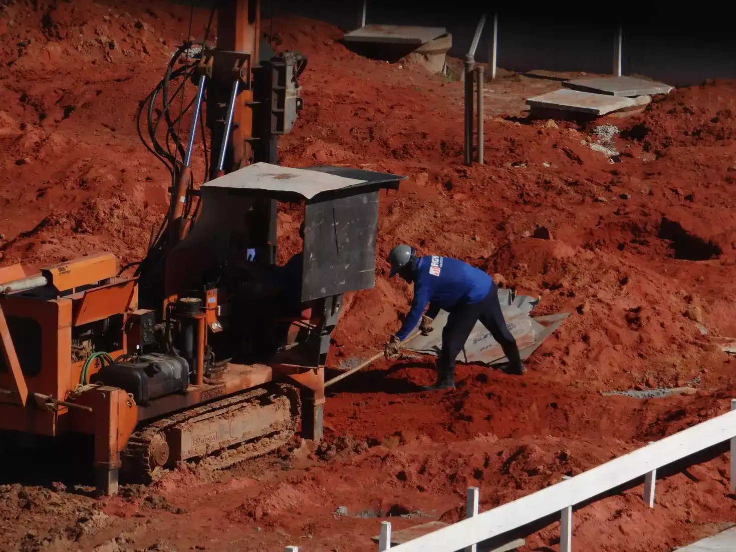 Operador trabajando junto a una perforadora sobre terreno rojizo