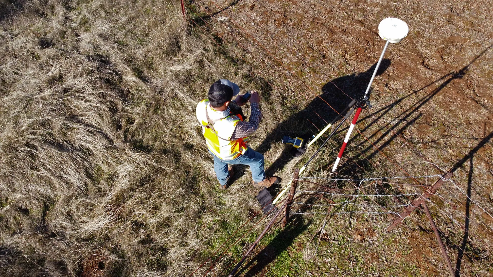 Topógrafo con ropa de alta visibilidad operando un receptor GNSS móvil en un sitio peruano