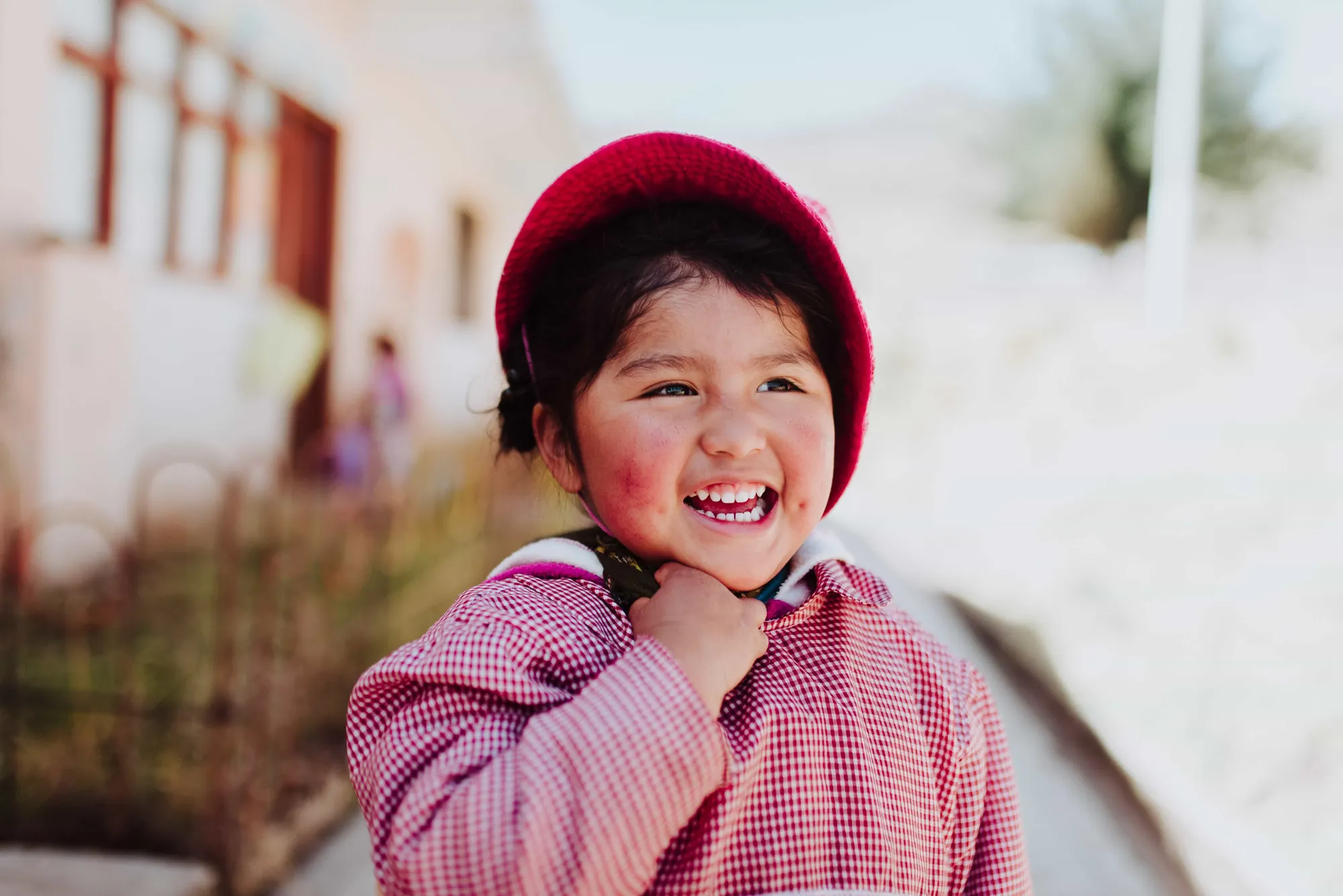 Una niña riendo con un gorro rojo frente a una escuela en la sierra peruana
