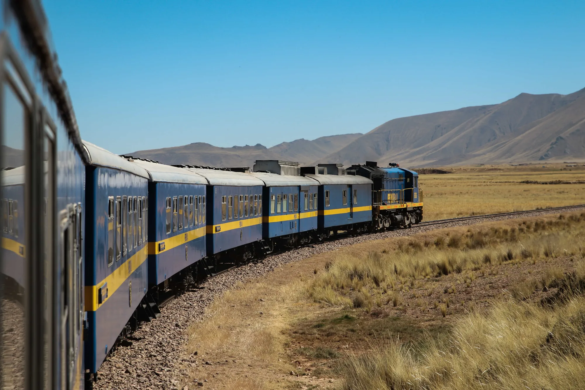 Tren de pasajeros trazando una curva por una pradera abierta con montañas al fondo