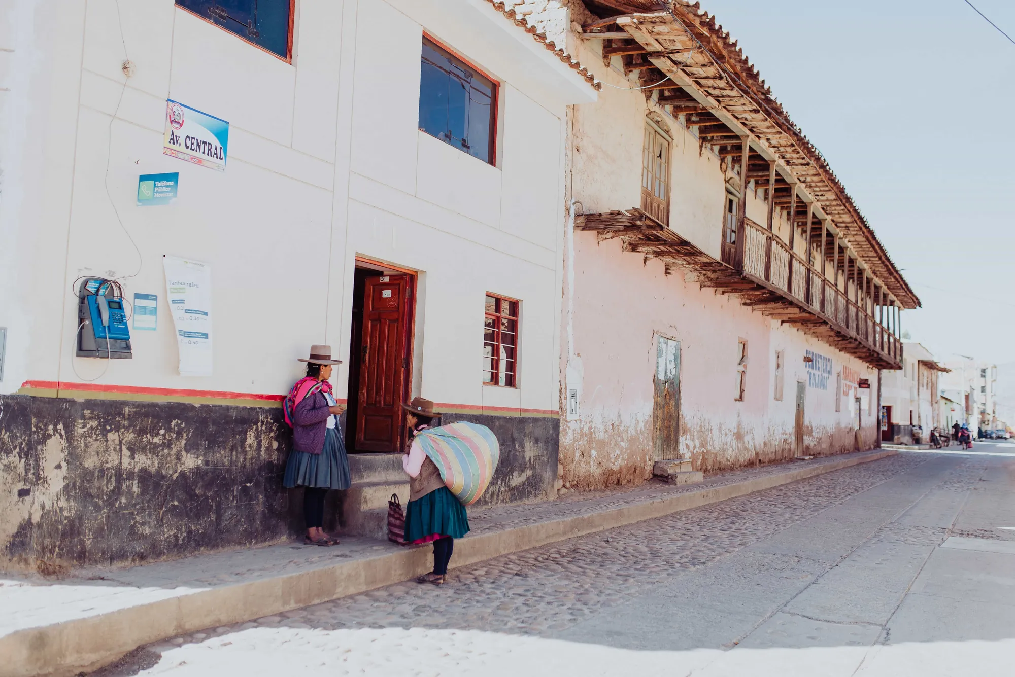 Dos mujeres frente a un edificio en la calle de un pueblo, una de ellas cargando un bulto