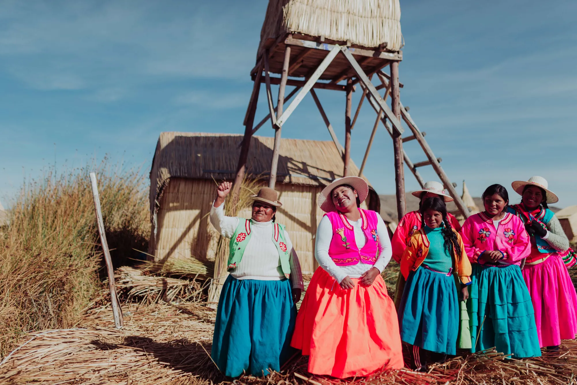 Grupo de mujeres con vestimenta tradicional reunidas al aire libre junto a una torre de totora
