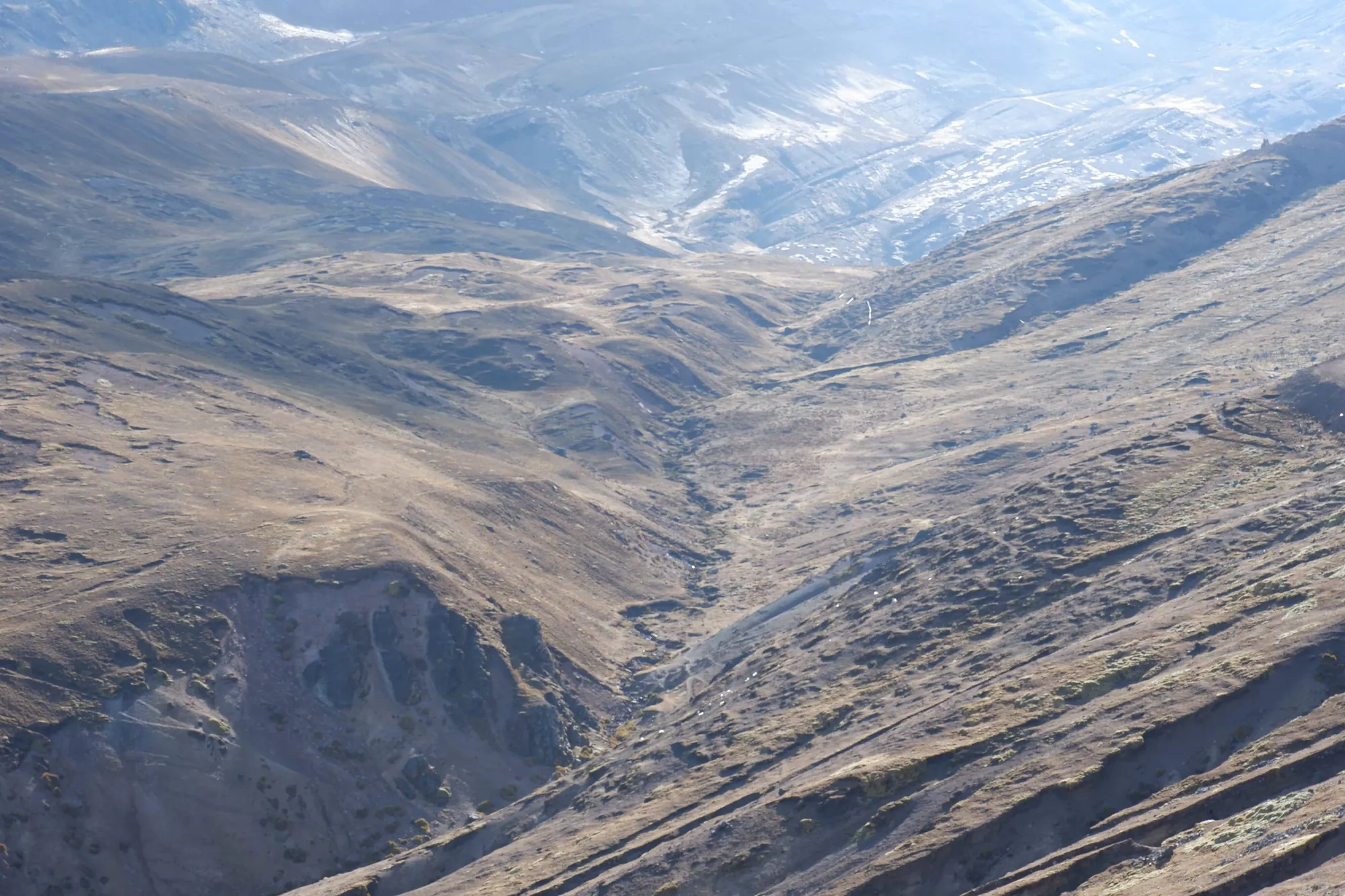 Vista aérea de un valle de montaña con manchas de nieve y laderas erosionadas