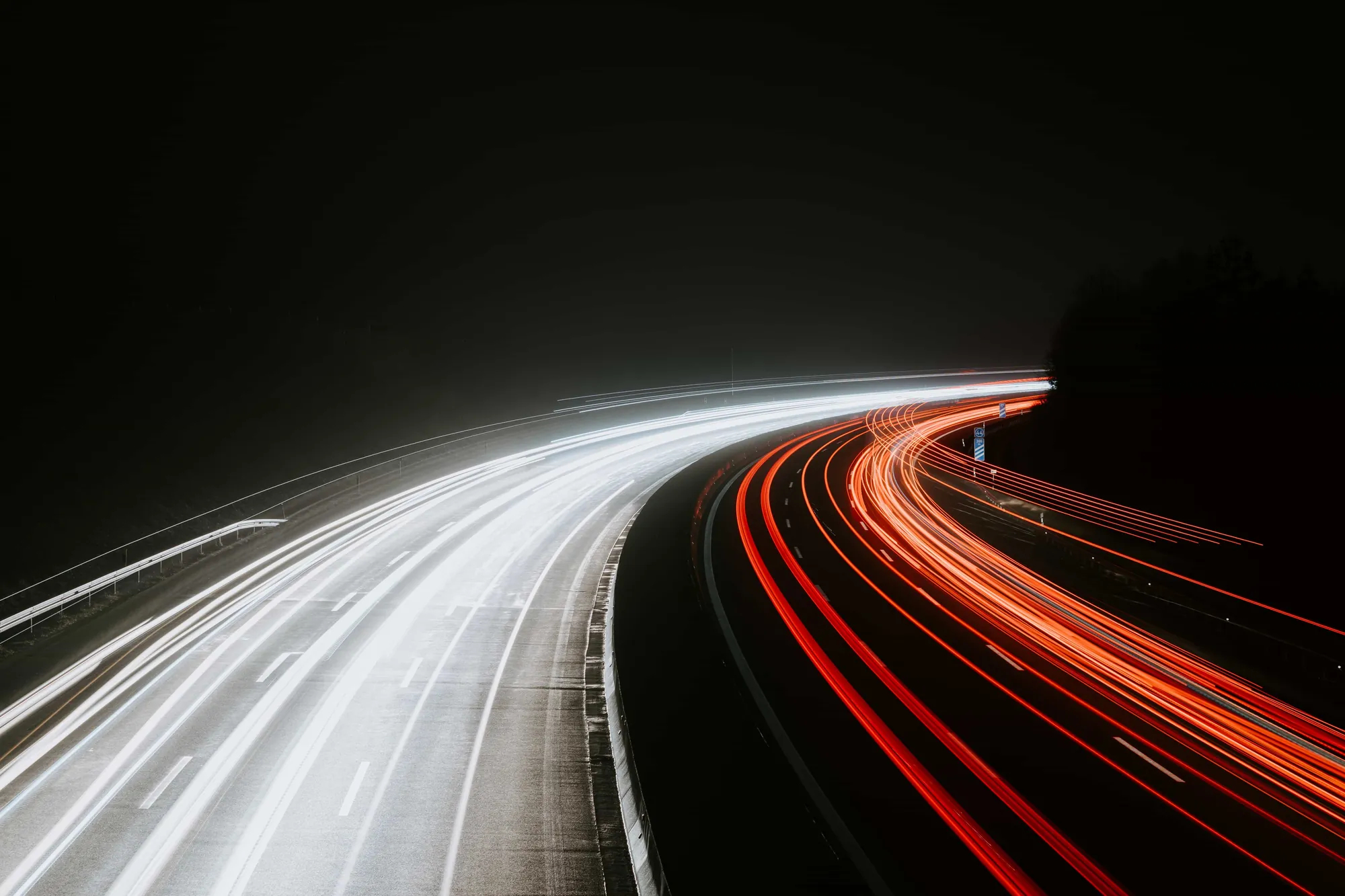 Exposición larga de estelas de luz de vehículos en una carretera con curvas de noche