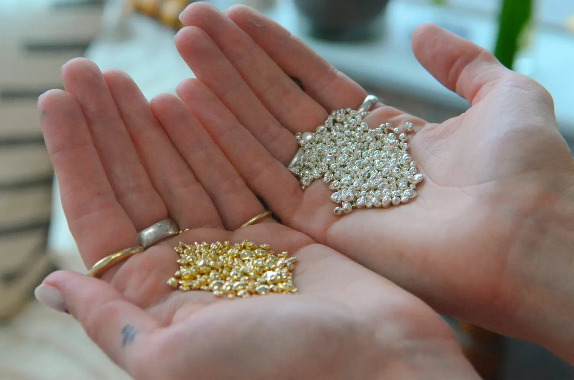 Manos sosteniendo pequeñas cantidades de gránulos de color oro y de color plata