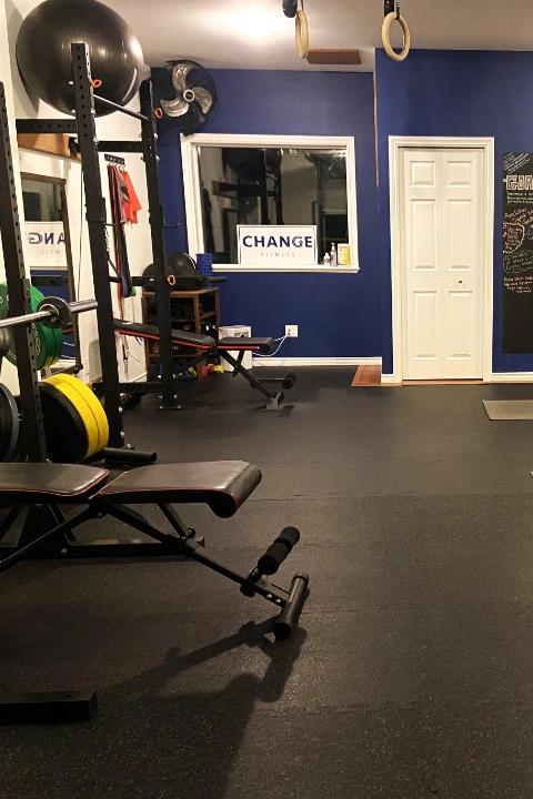 A fully equipped private fitness studio featuring a weight rack, exercise benches, dumbbell tower, kettlebells, and workout mats set up on black flooring.