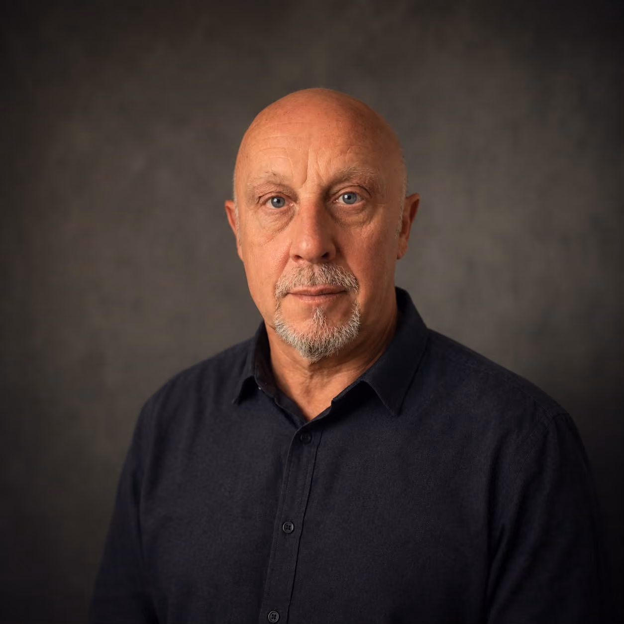 Portrait of a bald middle-aged man with a goatee wearing a dark button-up shirt.