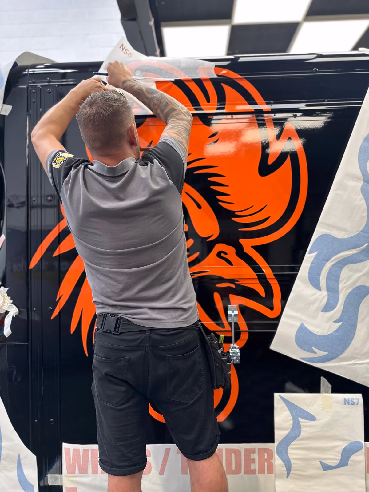 Man applying orange and black decal of an angry rooster on a black surface.