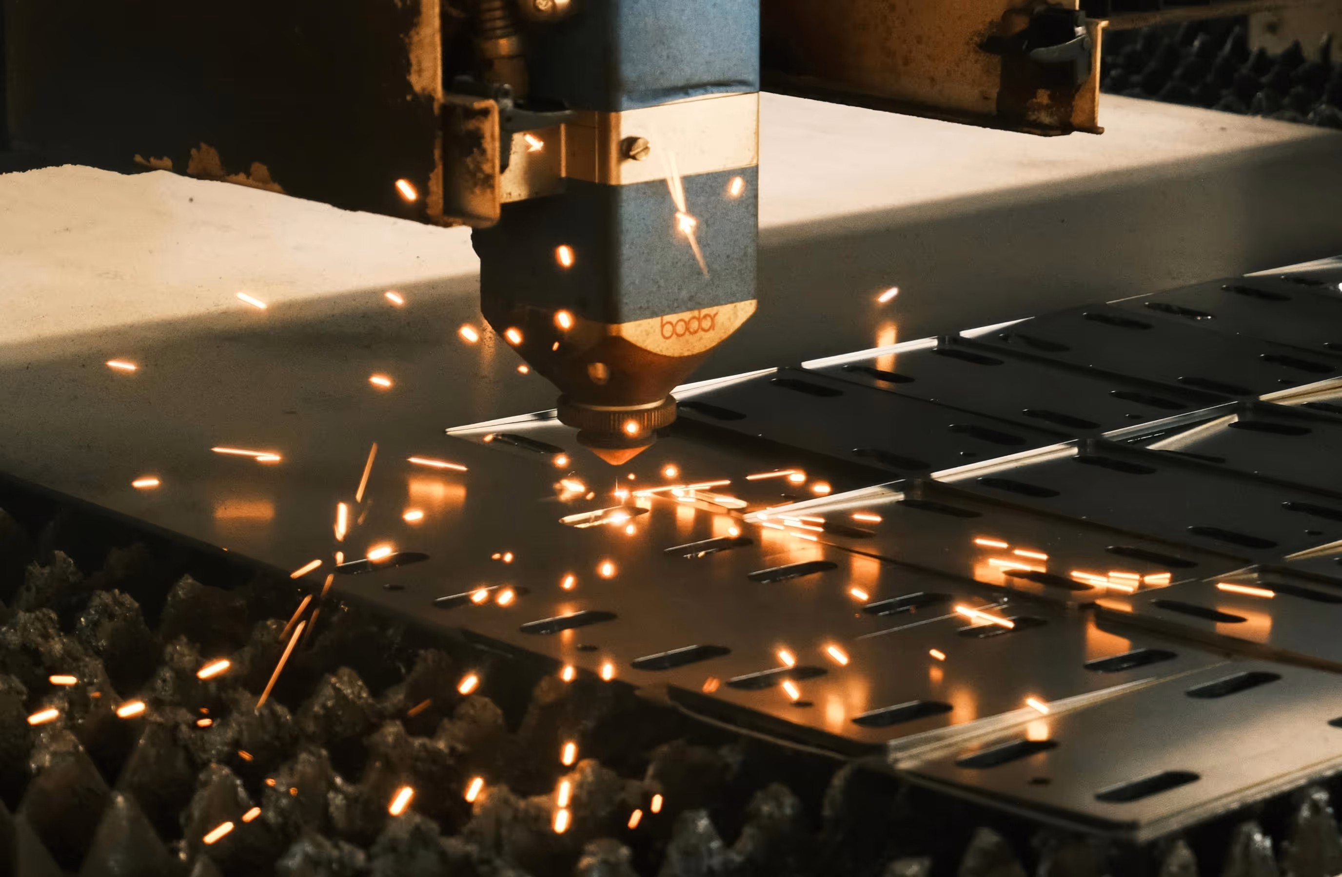 Close-up of a laser cutting machine making sparks while cutting rectangular shapes in a metal sheet.