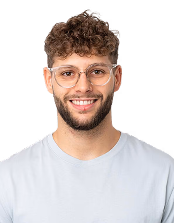 Smiling man with curly hair, beard, clear glasses, and a light shirt against a white background.