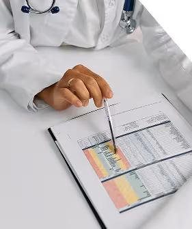 Medical professional in white coat pointing with a pen at a document with colorful charts and data tables.