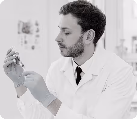 Male scientist in lab coat and gloves holding a syringe and vial in a laboratory setting.