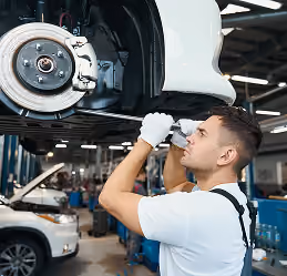 Mechanic in white shirt and gloves inspecting car brakes in a vehicle repair shop.