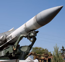 Large military missile mounted on a green launcher against a clear blue sky.