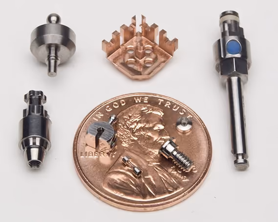 Various small metal mechanical components displayed around a US penny for size comparison.