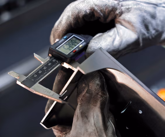 Gloved hand using digital caliper to measure thickness of metal sheet showing 2.90 mm.