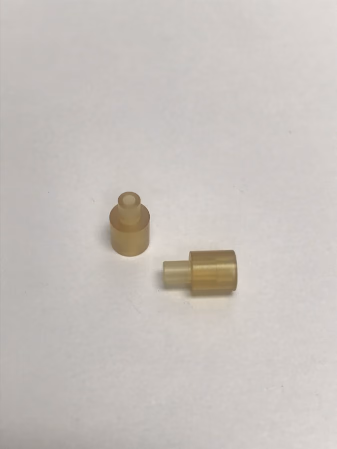 Two small translucent beige cylindrical plastic connectors on a white surface.